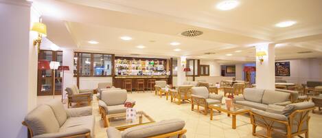 A hotel lobby with multiple seating areas, a bar, and a view of the city.