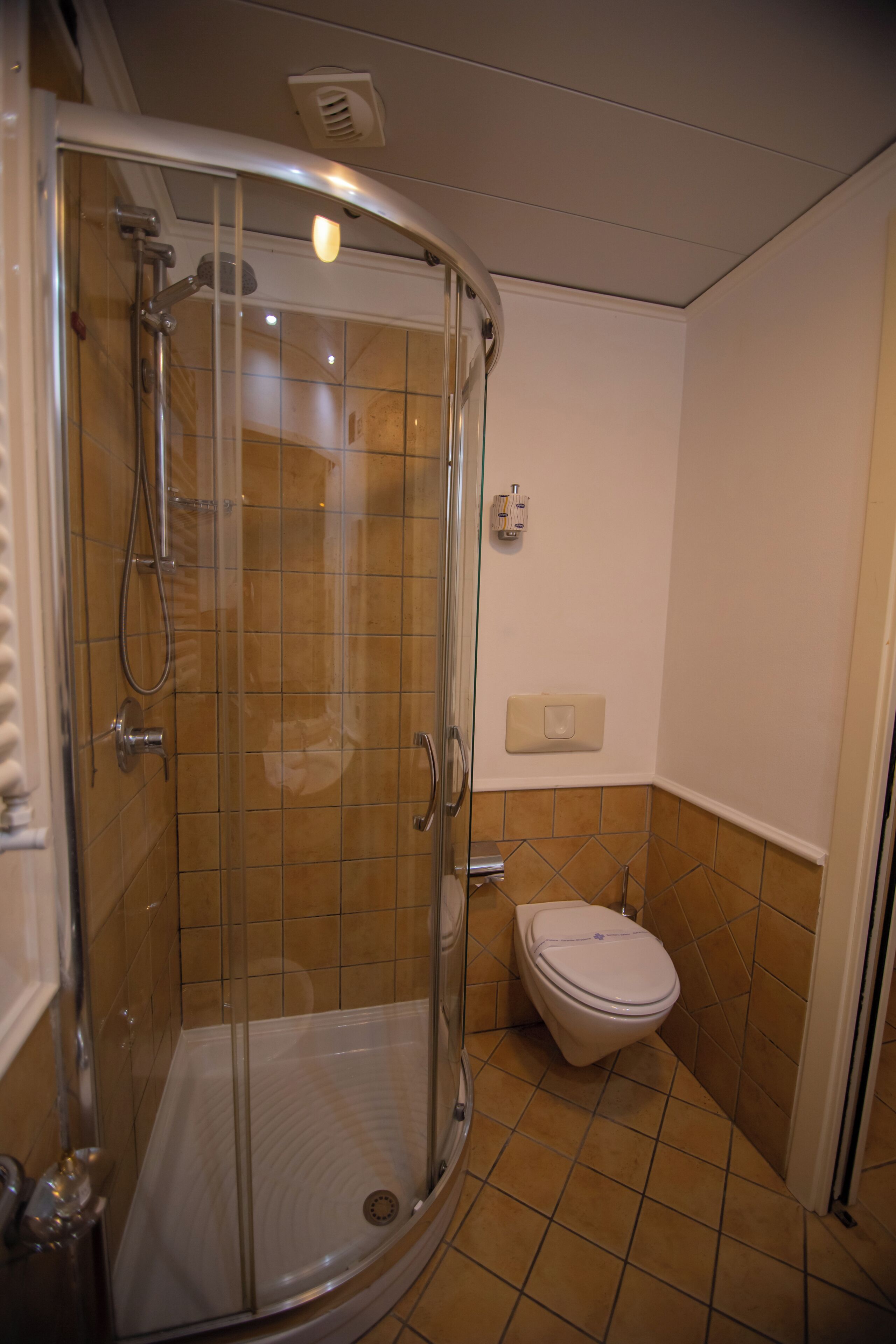 Un baño con ducha de vidrio, inodoro y secamanos de pared.