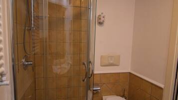Un baño con ducha de vidrio, inodoro y secamanos de pared.