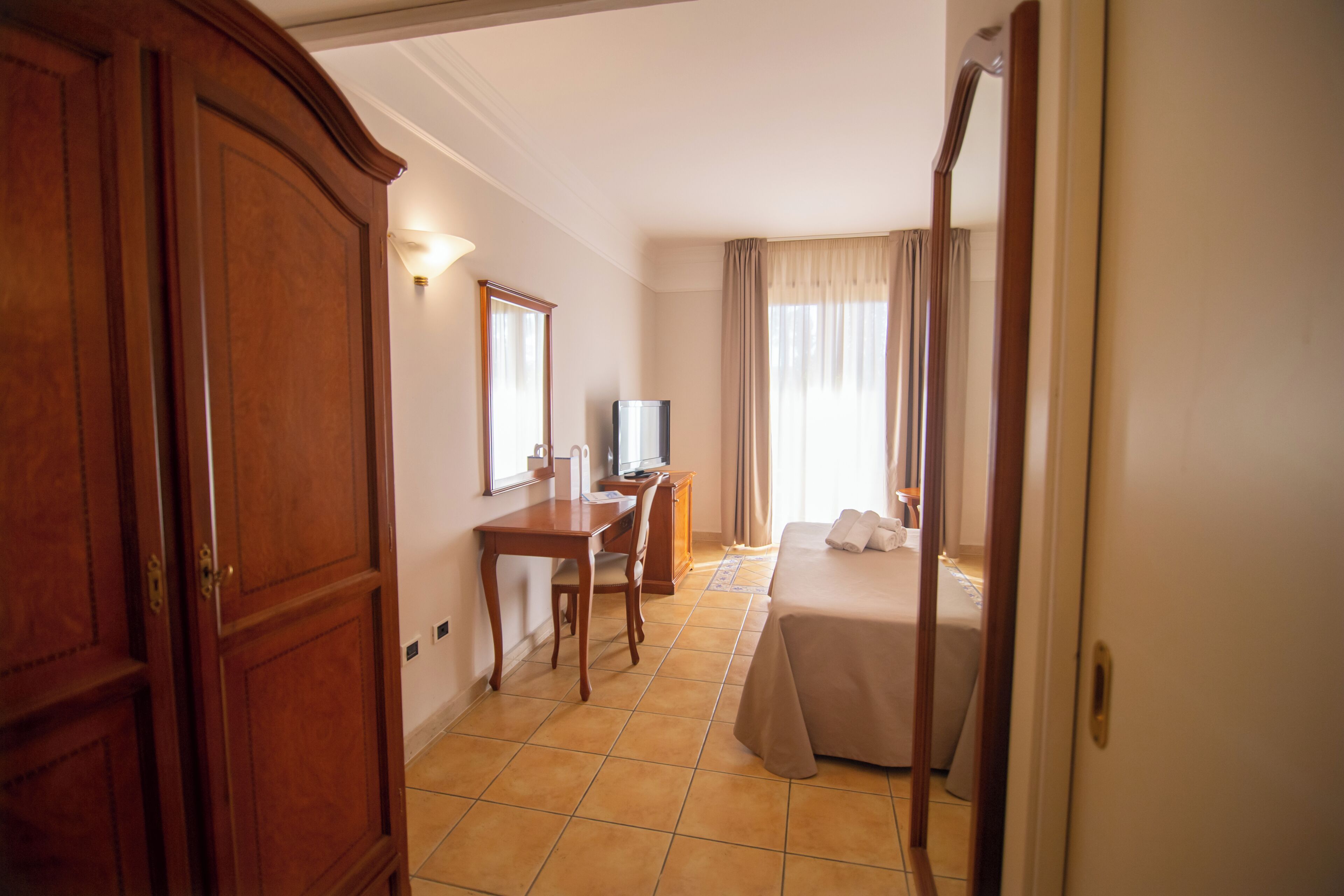 Une chambre d’hôtel avec une armoire en bois, un bureau avec une chaise, un lit et un téléviseur.