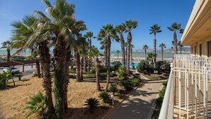 A balcony with a view of a sandy beach, palm trees, and a clear blue sky. - Dioscuri Bay Palace Hotel (Agrigento)