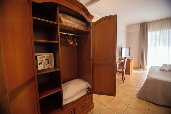 A hotel room with a wooden wardrobe, a bed, a desk, and a television. - Dioscuri Bay Palace Hotel (Agrigento)