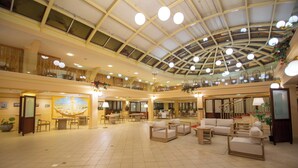 A spacious lobby with a high ceiling, multiple seating areas, and a large mural on the wall. - Dioscuri Bay Palace Hotel (Agrigento)