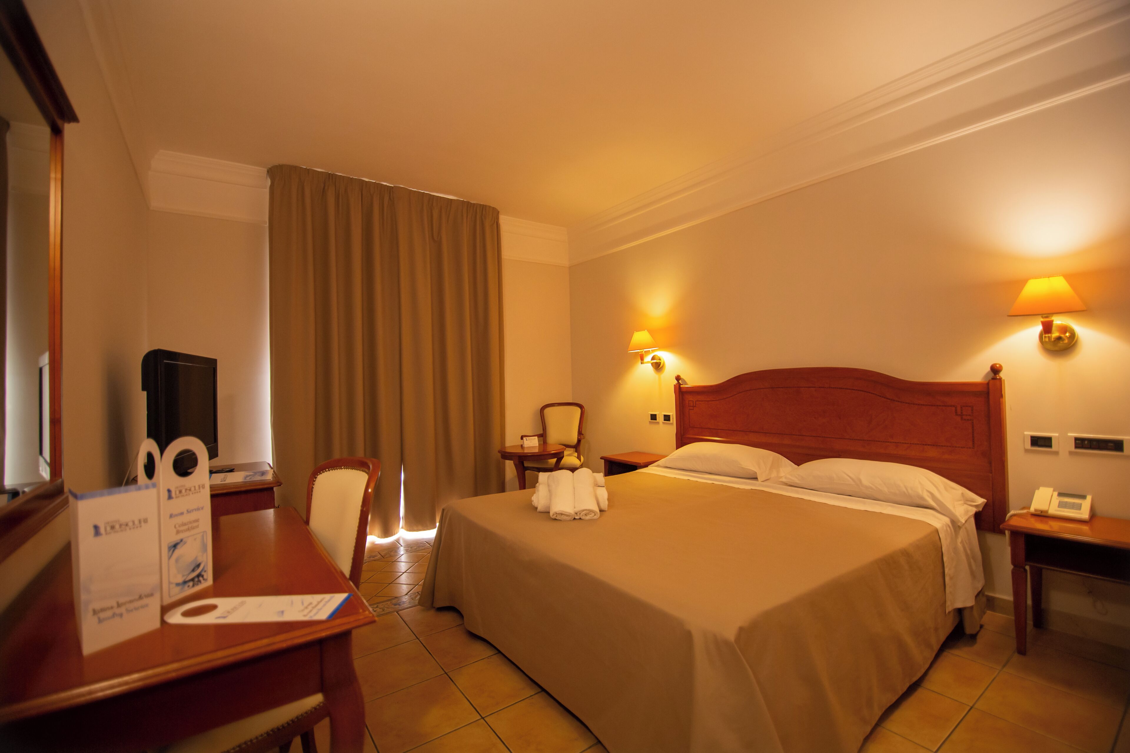 A hotel room with a bed, a desk with a chair, a television, and a lamp.