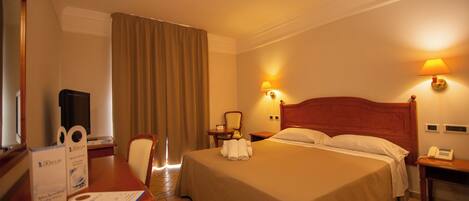 A hotel room with a bed, a desk with a chair, a television, and a lamp.