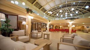 A spacious lobby with multiple seating areas, a high ceiling with a skylight, and a central dining area with red chairs. - Dioscuri Bay Palace Hotel (Agrigento)