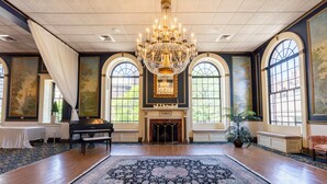 A grand room with a large chandelier, a piano, a fireplace, and a large ornate rug. - Inn on Broadway (Rochester)