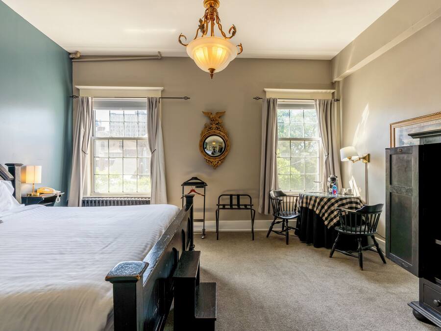 Une chambre d’hôtel avec un grand lit, un bureau avec une chaise, une cheminée et un miroir au mur.