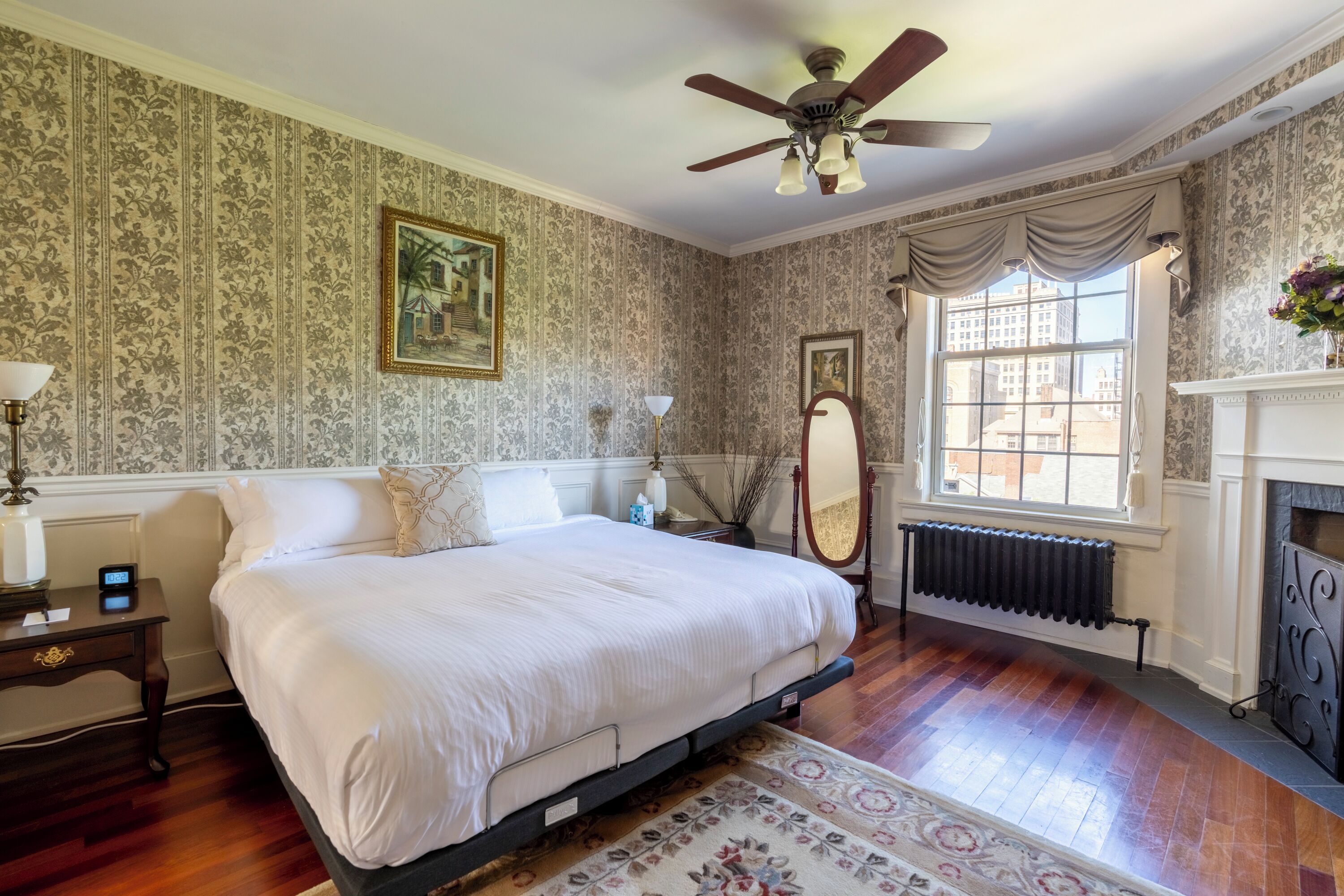 A bedroom with a large bed, a ceiling fan, a fireplace, and a window with curtains.