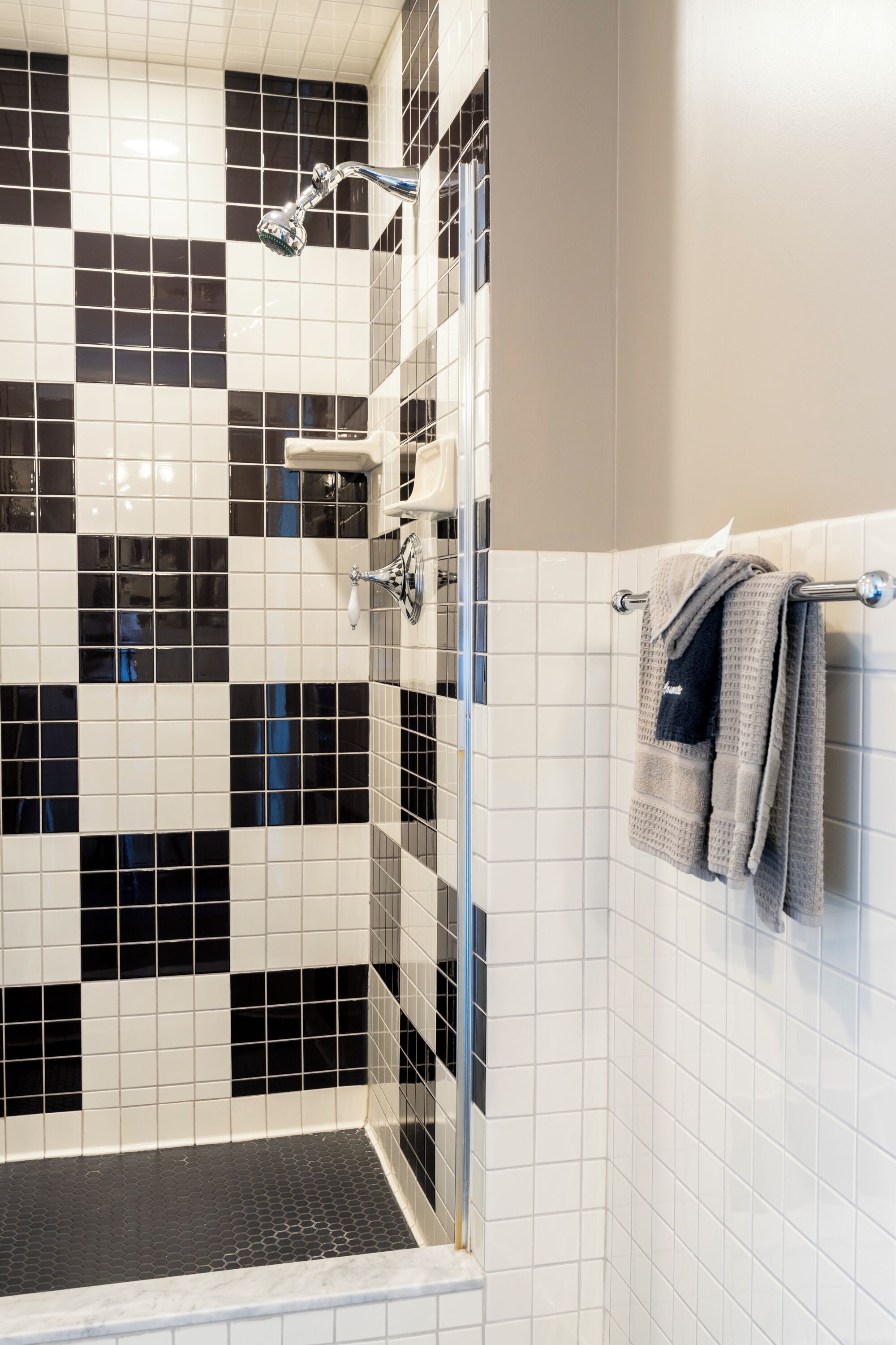 Une douche aux carreaux noirs et blancs, une porte en verre et un porte-serviettes avec des serviettes.