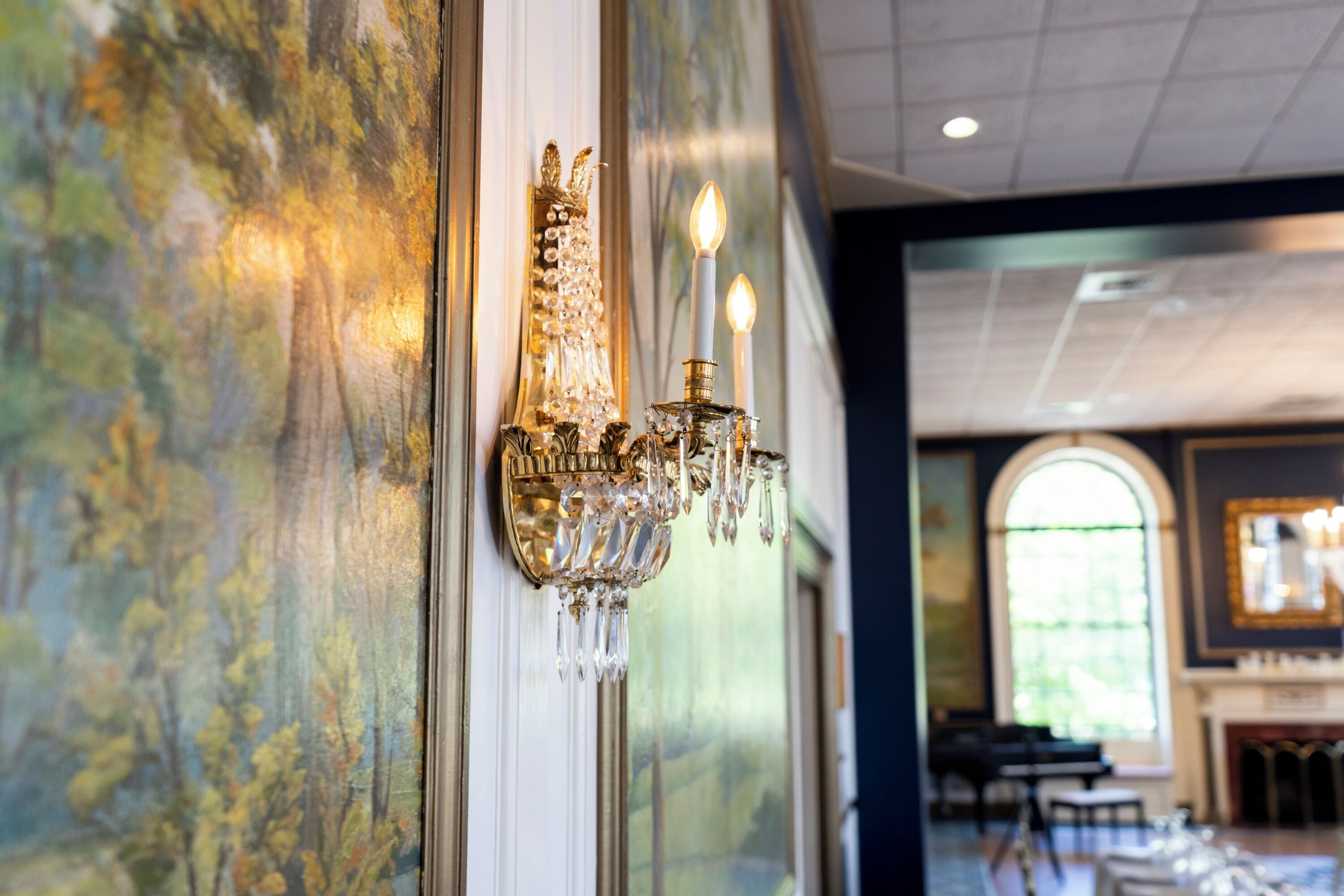 Un candelabro con múltiples velas, un cuadro en la pared y vista de una habitación con mesas y sillas.