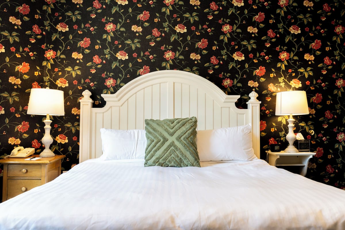 A neatly made bed with white linens, a green pillow, and two bedside tables with lamps.