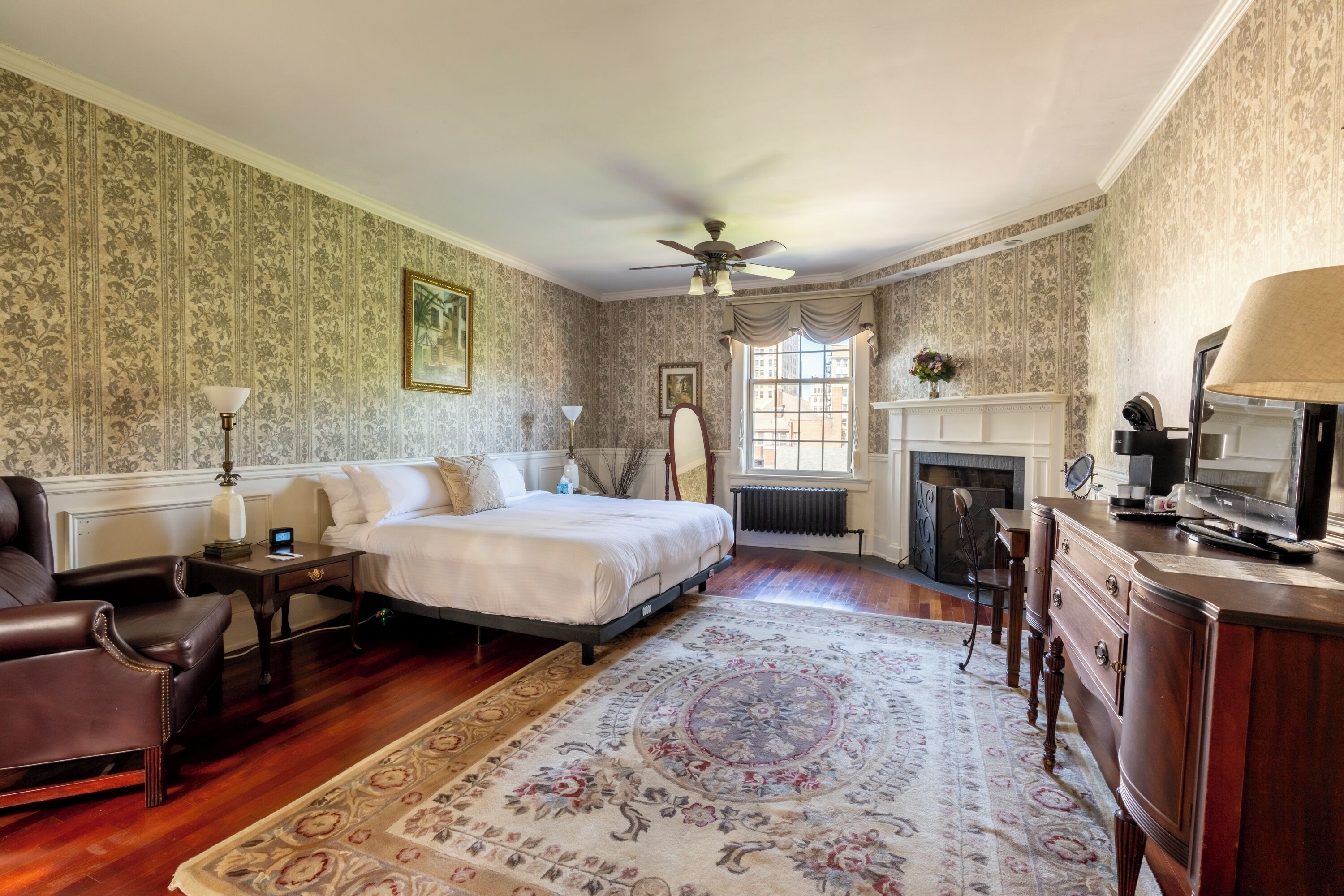 A bedroom with a bed, a desk, a chair, a fireplace, and a television.