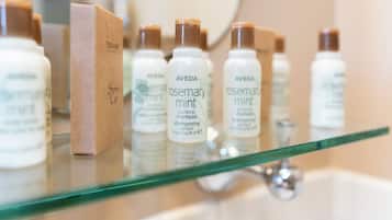 A bathroom shelf with various Aveda products, including a box and several bottles of shampoo.