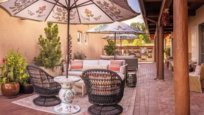 An outdoor patio with wicker furniture, a table, and two umbrellas providing shade.