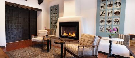 A cozy living room with a fireplace, striped chairs, a coffee table, and a wall decorated with framed artwork.