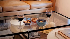 A glass-top coffee table with bowls, wine glasses, and books in a living room with a leather couch.