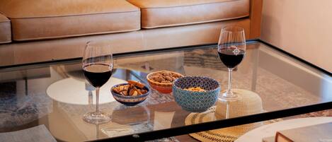 A glass-top coffee table with bowls, wine glasses, and books in a living room with a leather couch.