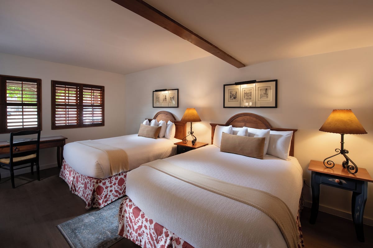 A bedroom with two beds, a desk, and two lamps.