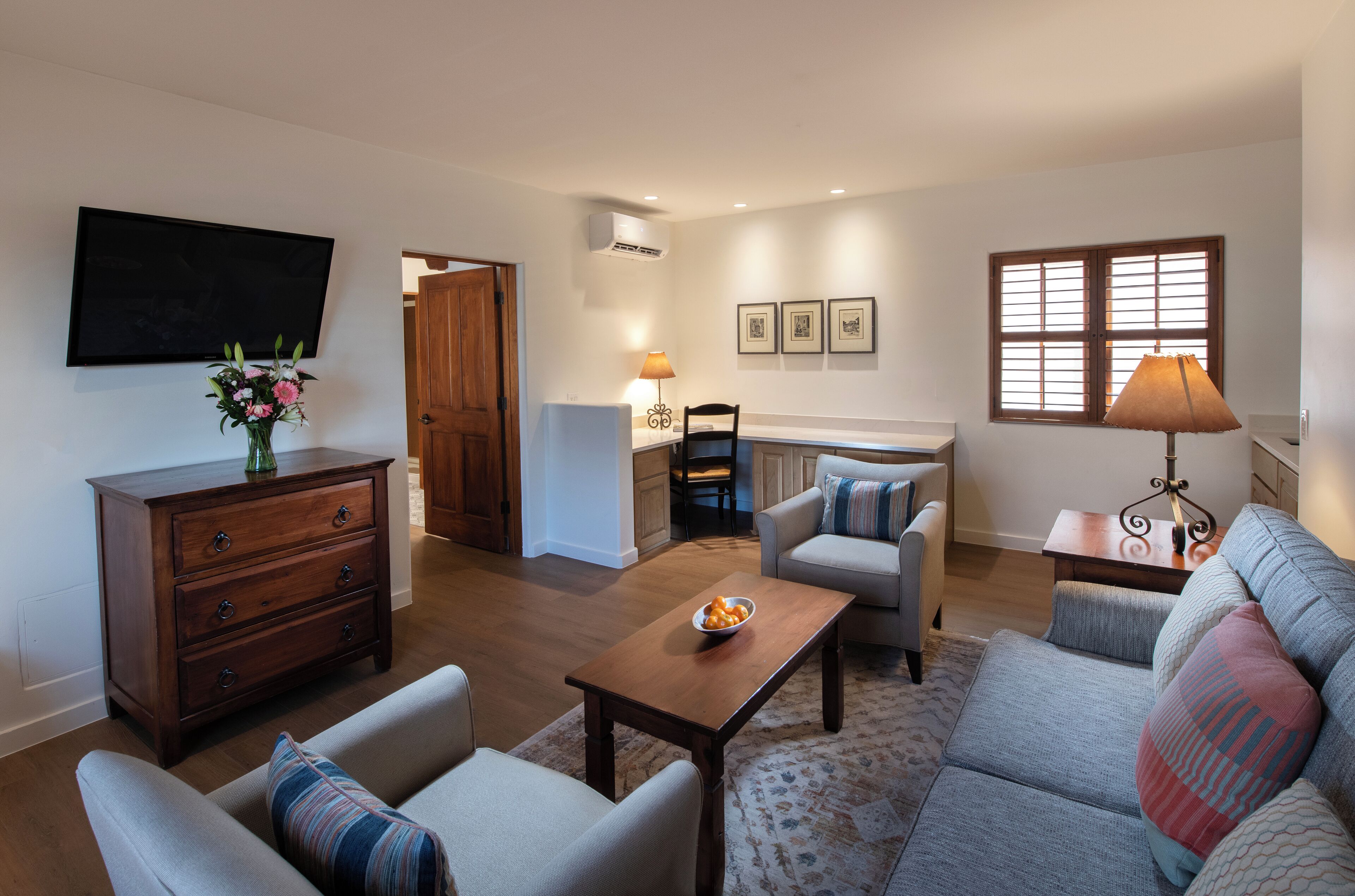 Un salon comprenant un canapé, des fauteuils, une table basse et un téléviseur. On y trouve également une commode en bois et une lampe sur une table d’appoint.