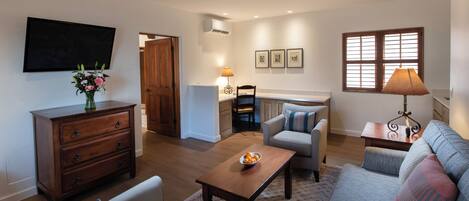 Un salon comprenant un canapé, des fauteuils, une table basse et un téléviseur. On y trouve également une commode en bois et une lampe sur une table d’appoint.