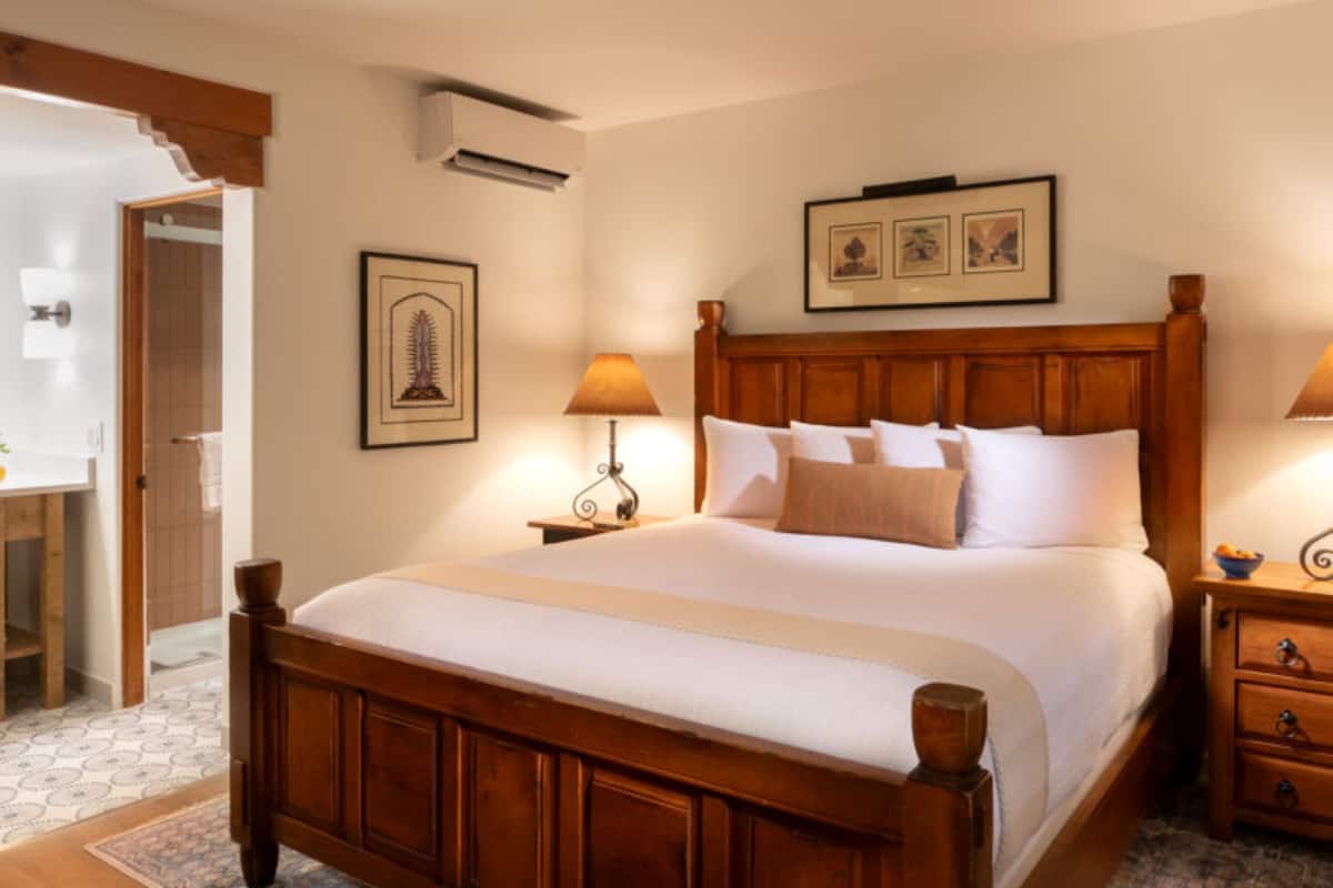 A large wooden bed with a headboard, two bedside tables with lamps, a framed picture above the bed, and a patterned rug.