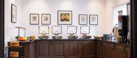 A kitchen with wooden cabinets, a brick floor, and a countertop with various kitchen items and framed pictures on the wall.