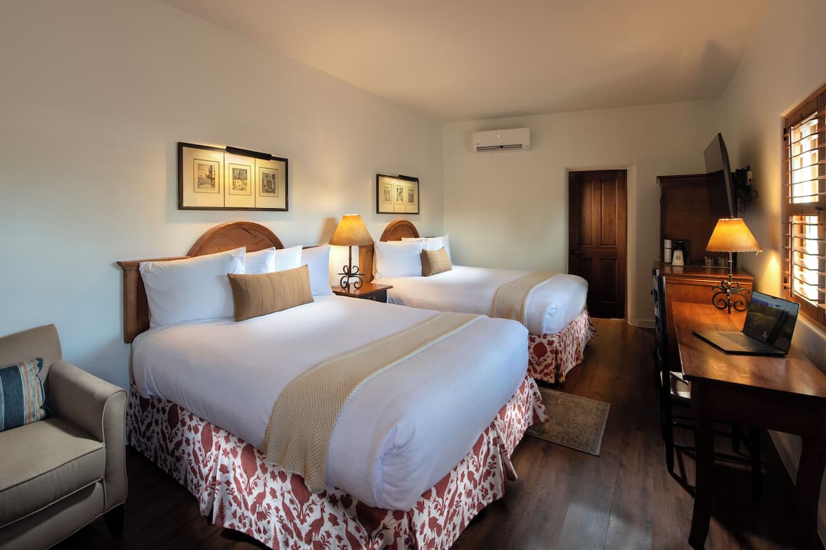 A hotel room with two beds, a desk with a laptop, a chair, a sofa, and framed pictures on the wall.