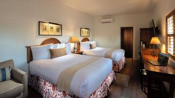 A hotel room with two beds, a desk with a laptop, a chair, a sofa, and framed pictures on the wall.