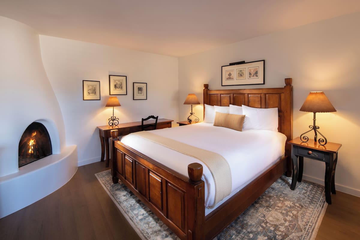 A neatly arranged bedroom with a large bed, a fireplace, and two bedside tables with lamps.