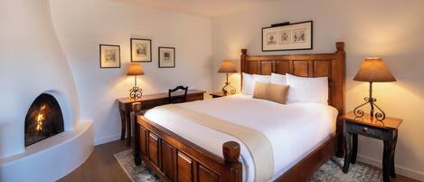 A neatly arranged bedroom with a large bed, a fireplace, and two bedside tables with lamps.