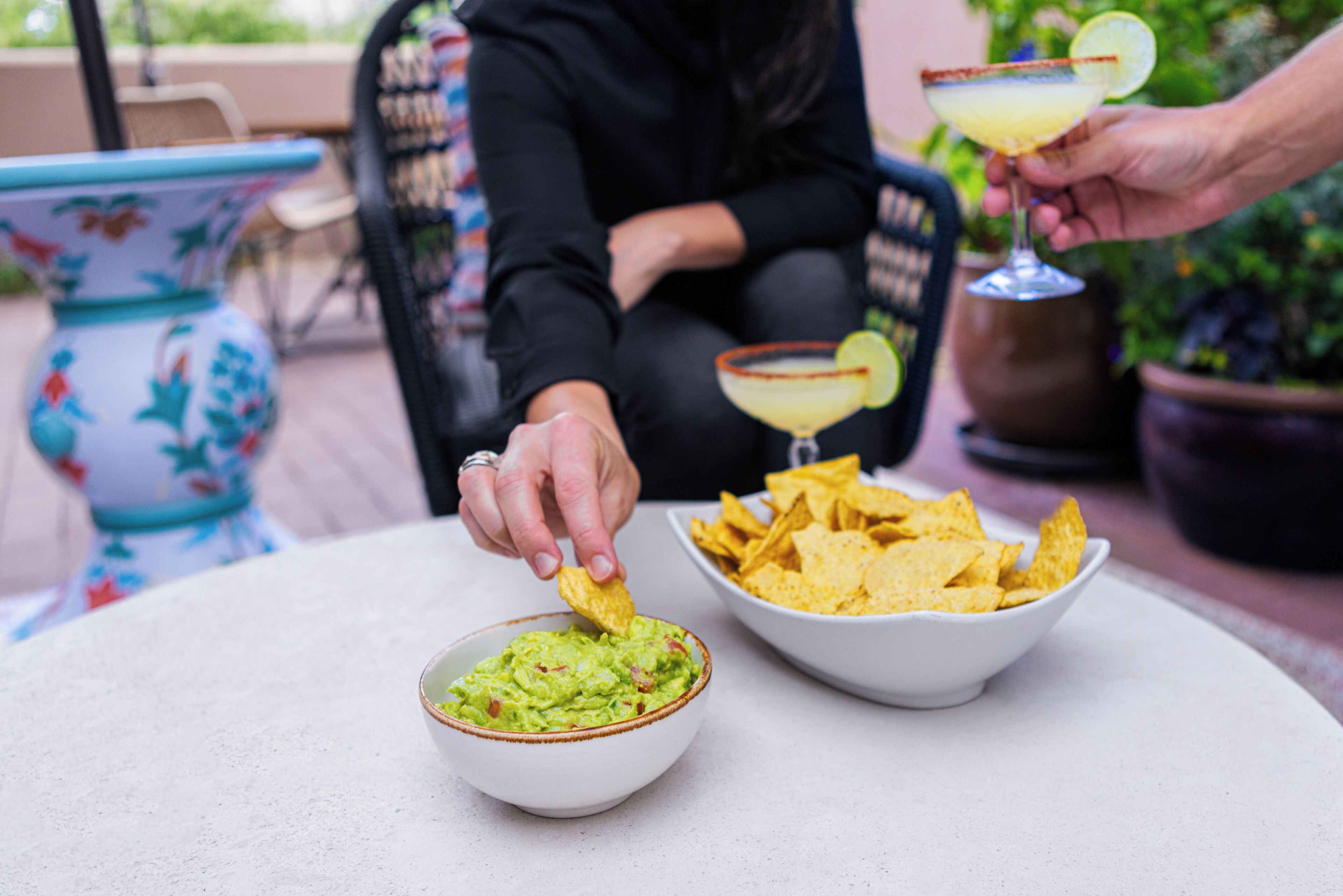 Una persona submergeix una patata en un bol de guacamole, amb una margarita i un altre bol de patates al fons.