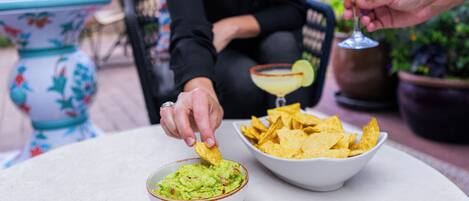 Una persona submergeix una patata en un bol de guacamole, amb una margarita i un altre bol de patates al fons.