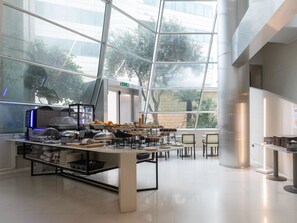 A modern dining area with a glass partition, a coffee machine, and a variety of food items on display. - B&B Hotel Trapani Crystal (Trapani)