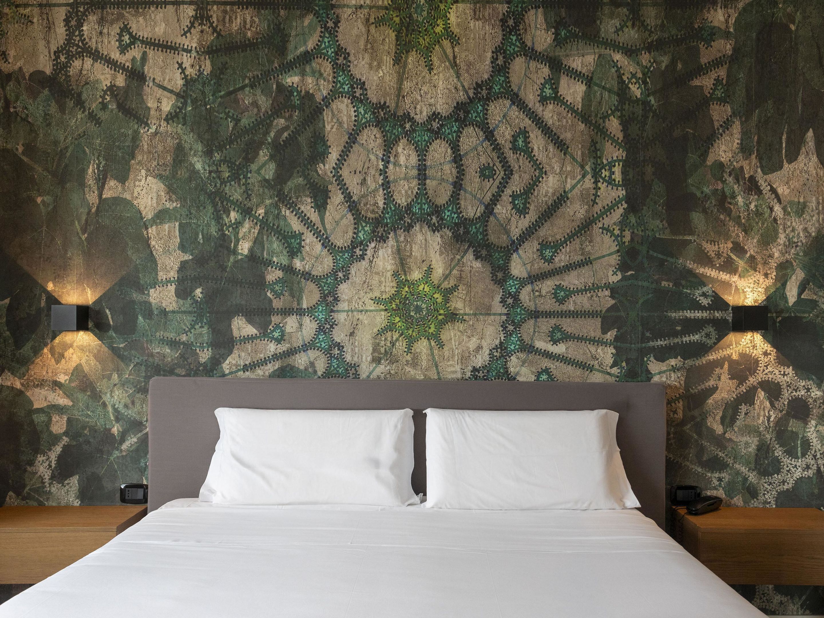 Hotelkamer met een groot bed, een hoofdeinde, twee nachtkastjes en een muur met een ingewikkeld geometrisch patroon.