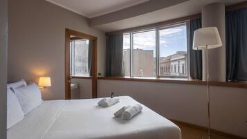 Une chambre d’hôtel avec un lit bien fait, un lampadaire et une fenêtre donnant sur la ville.