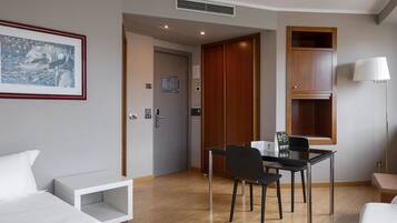 Habitación de hotel con cama, escritorio y silla, un cuadro en la pared, un armario de madera y una lámpara.