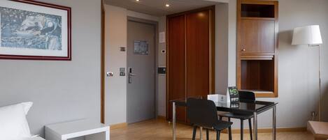 A hotel room with a bed, a desk with a chair, a framed picture on the wall, a wooden cabinet, and a lamp.