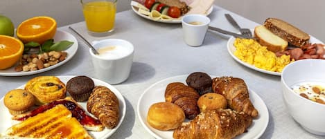 A breakfast table with various food items including pastries, bread, and a glass of orange juice.