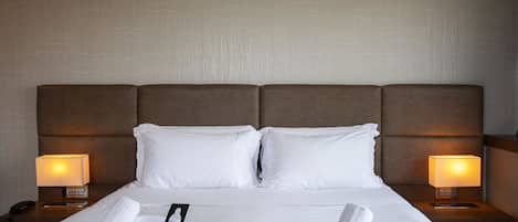 A hotel room with a large bed, two bedside lamps, and neatly folded towels on the bed.