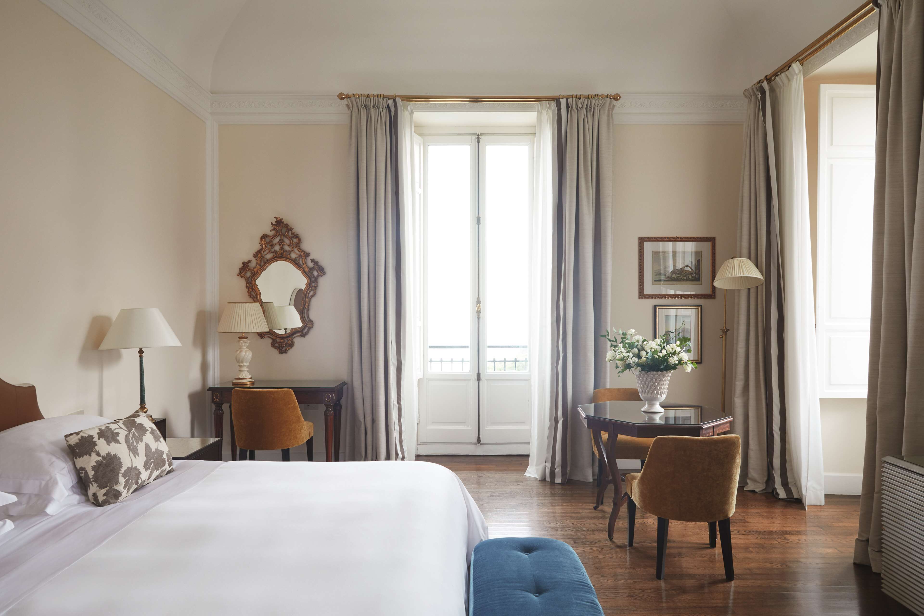 Ein Hotelzimmer mit Bett, zwei Stühlen, einem Tisch, einem Spiegel und einem Fenster mit Vorhängen.
