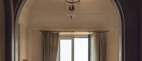 A hotel room with a bed, a chair, a desk, and a view of the sea through a large window.