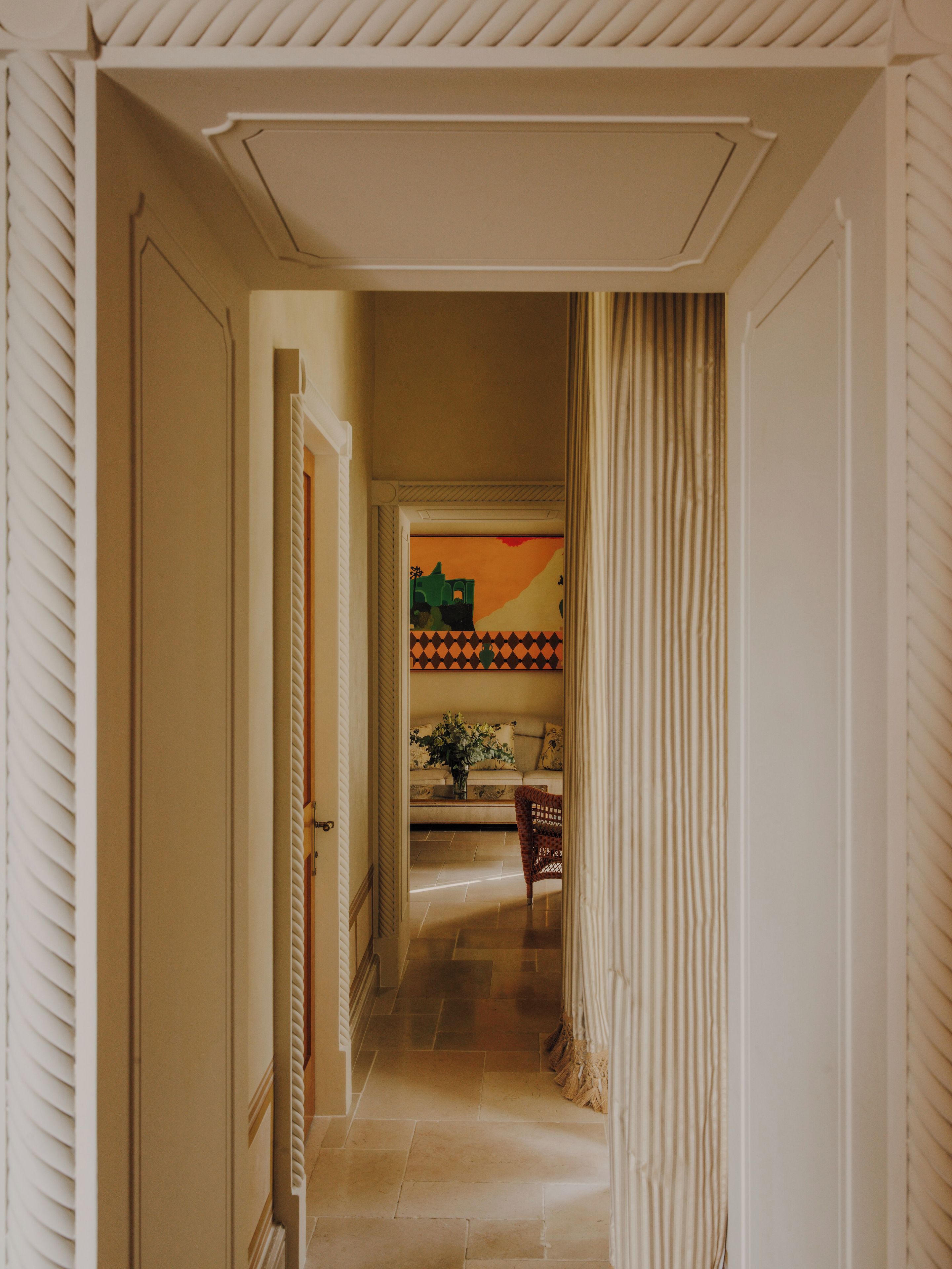 A hallway with a door leading to a room, a chair, and a table with a vase of flowers.