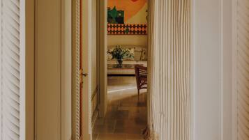 A hallway with a door leading to a room, a chair, and a table with a vase of flowers.