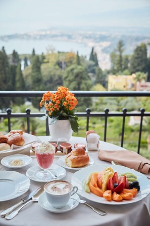 Una mesa servida con pasteles, fruta y una bebida, con vistas a un paisaje pintoresco.