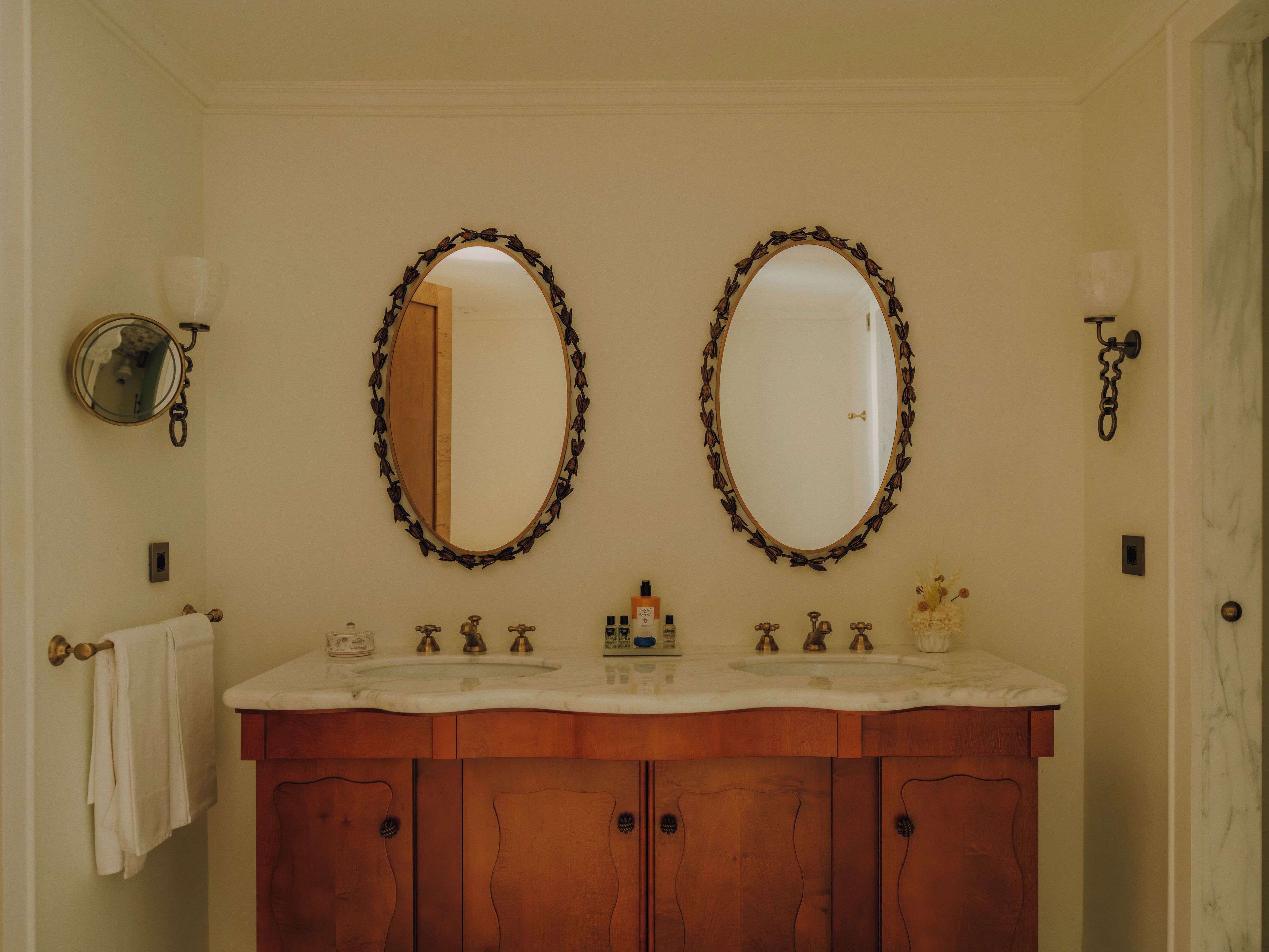 A bathroom with two oval mirrors, a wooden vanity, and a towel rack.