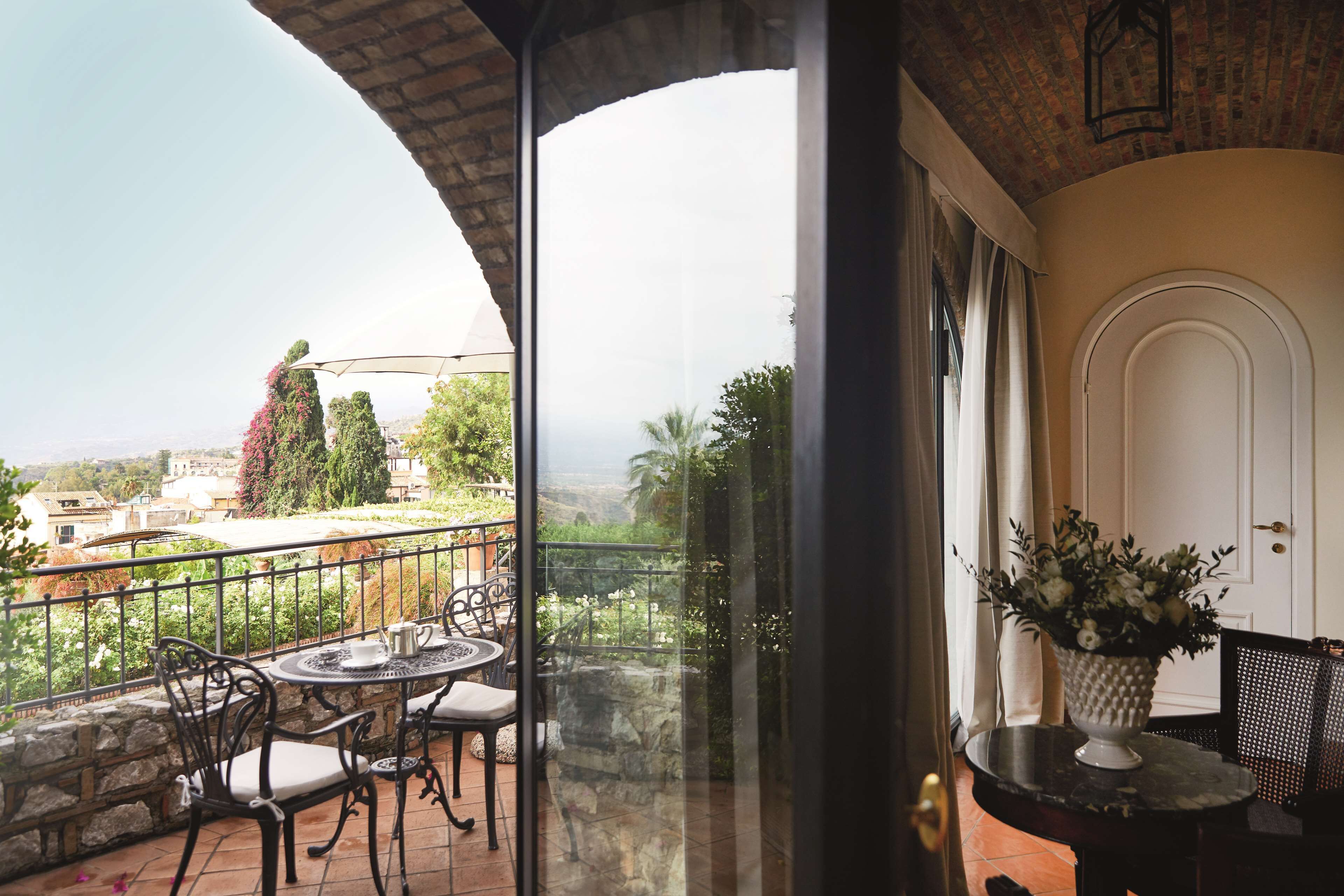 A balcony with a table and chairs, a potted plant, and a view of the landscape.