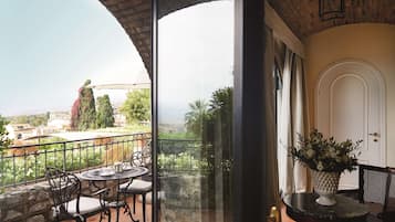 A balcony with a table and chairs, a potted plant, and a view of the landscape.