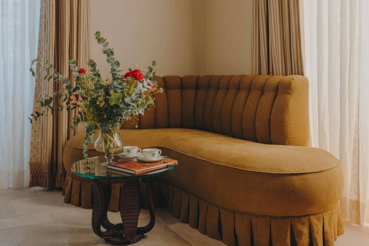 Una sala de estar acogedora con un sofá marrón, una mesa de centro de vidrio y un florero, y una lámpara de pared.