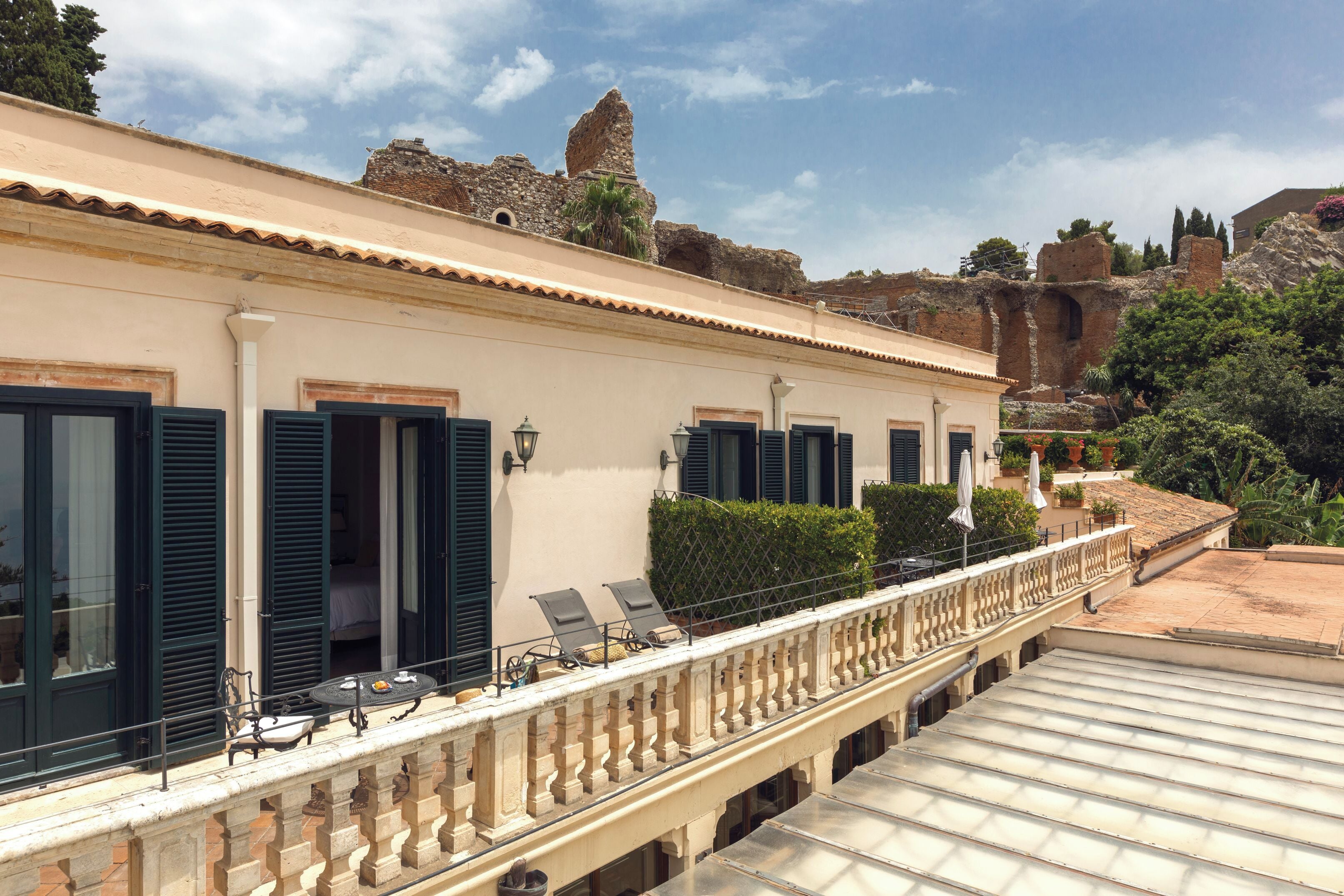 Un hotel con balcón, mobiliario exterior y vistas a ruinas antiguas.